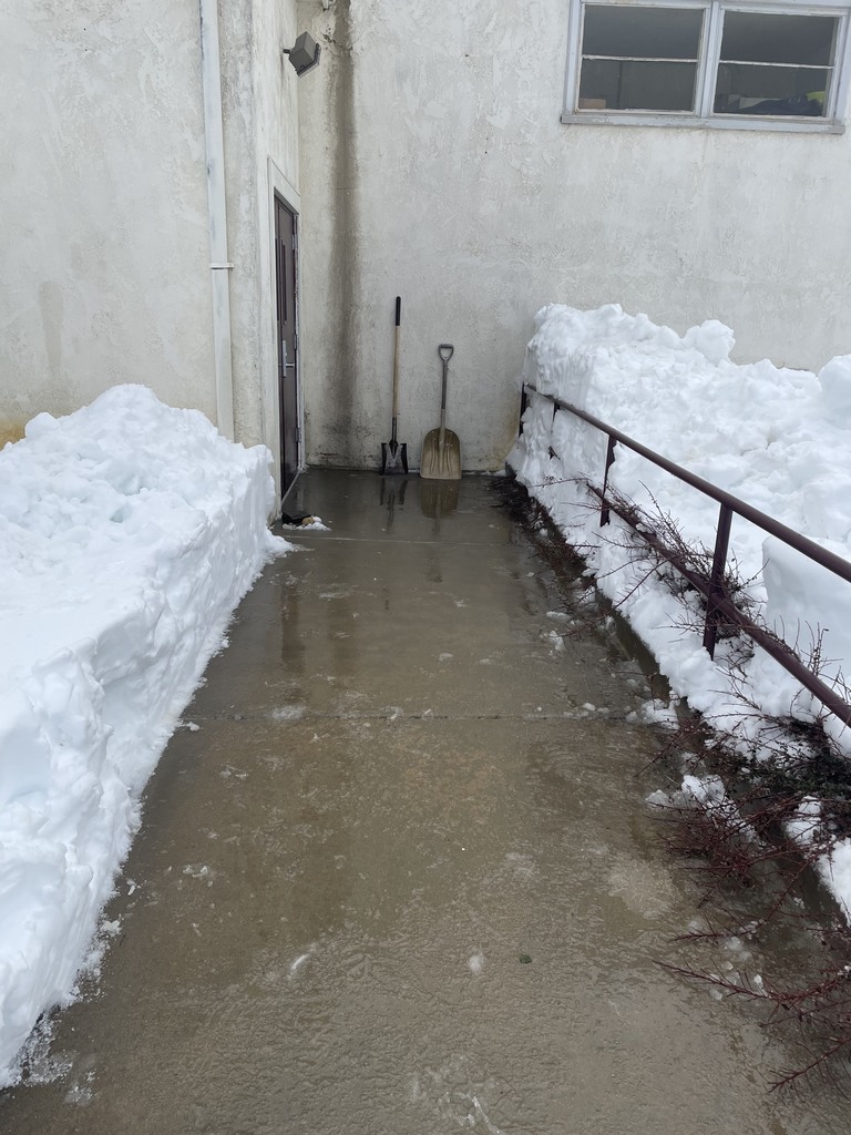 Snow has been shoveled away from the door. Two shovels rest against the wall.